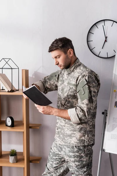 Serious military man holding notepad near wooden rack — Stock Photo