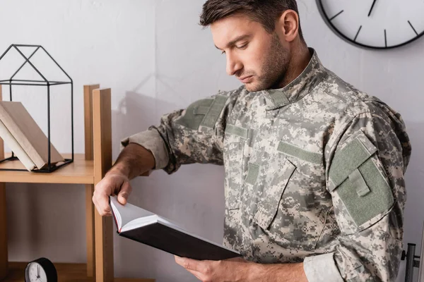 Militar serio en uniforme sujetando bloc de notas cerca de estante de madera - foto de stock