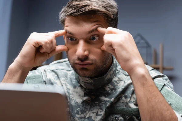 Müder Soldat in Uniform blickt auf Laptop im verschwommenen Vordergrund — Stockfoto
