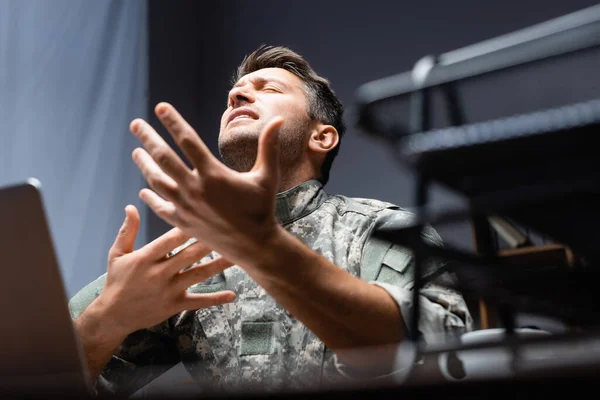 Militar en un gesto uniforme mientras expresa sentimientos cerca de bandeja de documento borrosa en el fondo - foto de stock