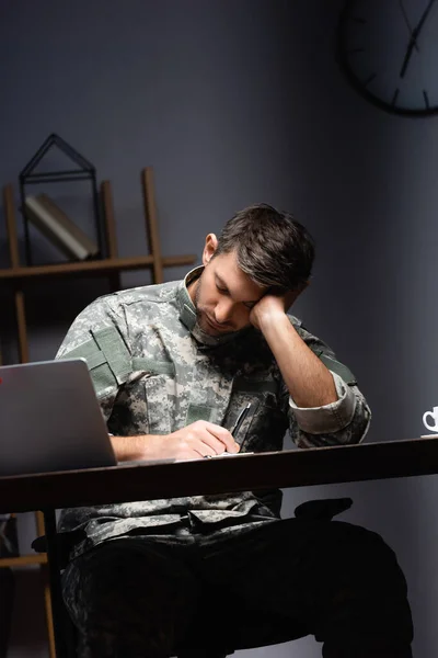 Militar cansado en uniforme durmiendo cerca de la computadora portátil en la oficina - foto de stock