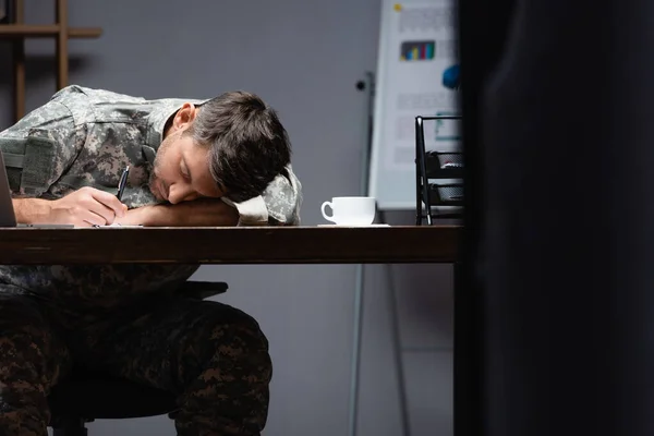 Militar cansado en uniforme durmiendo cerca de la taza en la oficina - foto de stock