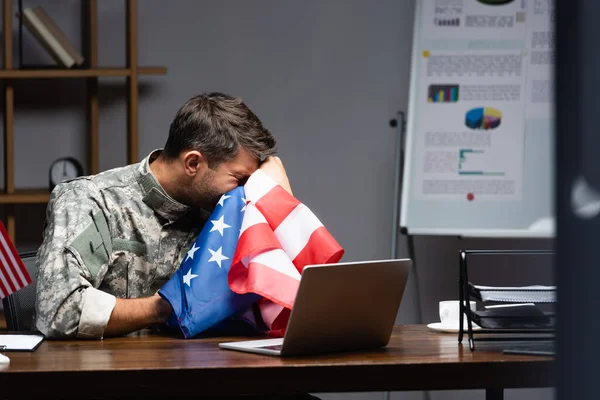 Militärangehöriger in Uniform weint und verhüllt Gesicht mit Amerika-Flagge in der Nähe des Laptops — Stockfoto