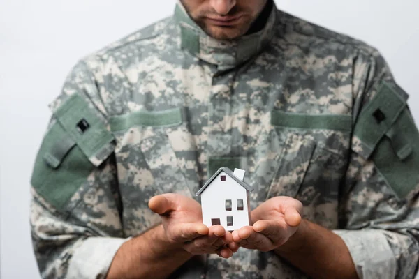 Hausmodell in den Händen patriotischer Militärs in Uniform auf verschwommenem Hintergrund isoliert auf weißem Hintergrund — Stockfoto