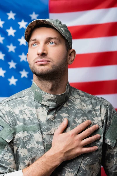 Patriótico militar homem jurando fidelidade perto de bandeira americana em fundo turvo — Fotografia de Stock