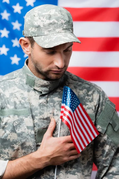 Patriotic military man in uniform and cap holding small american flag on blurred background — Stock Photo
