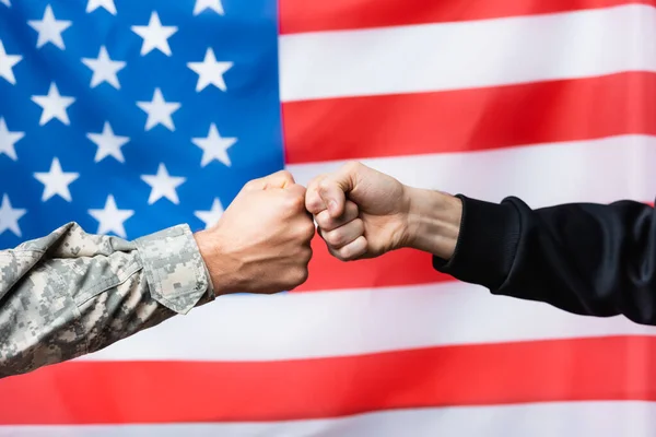 Ausgeschnittene Ansicht von Soldat, der mit Zivilmann nahe der amerikanischen Flagge auf verschwommenem Hintergrund zusammenstößt — Stockfoto