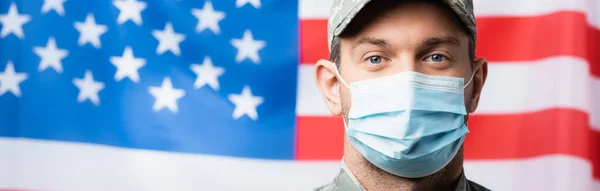 Homem militar patriótico em uniforme e máscara médica perto da bandeira americana em fundo borrado, bandeira — Fotografia de Stock