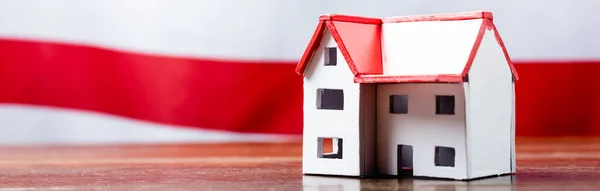 Modelo da casa perto de bandeira despojado vermelho no fundo borrado, banner — Fotografia de Stock