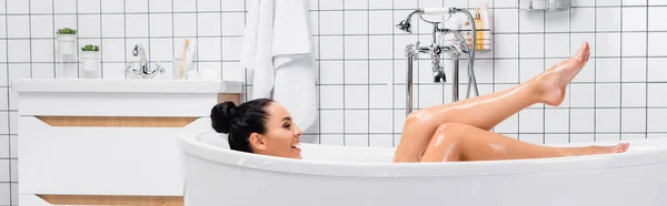 Усміхнена жінка дивиться на мокрі ноги, приймаючи ванну, банер — стокове фото