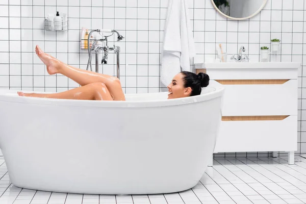 Lächelnde Frau blickt beim Baden zu Hause auf feuchte Beine — Stockfoto