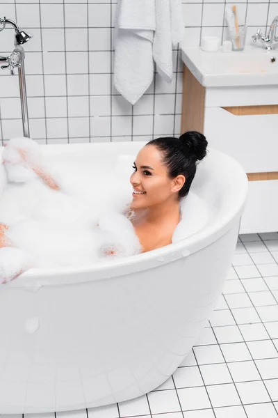 Joven mujer alegre bañándose con espuma en la bañera - foto de stock