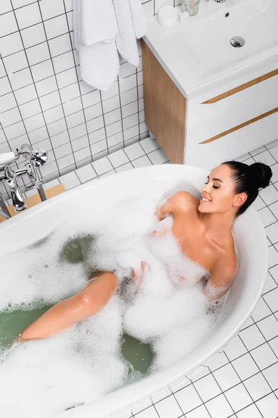 Vue de dessus de la femme sensuelle souriant tout en se relaxant dans la baignoire avec mousse — Photo de stock