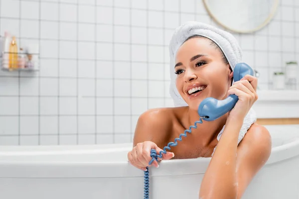 Mujer joven con toalla en la cabeza hablando por teléfono en la bañera - foto de stock