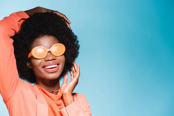 Smilig african american young woman in orange stylish outfit isolated on blue background — Stock Photo
