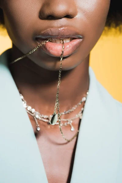 Vista ritagliata della giovane donna afroamericana in abito elegante blu con collana in bocca isolata sul giallo — Foto stock