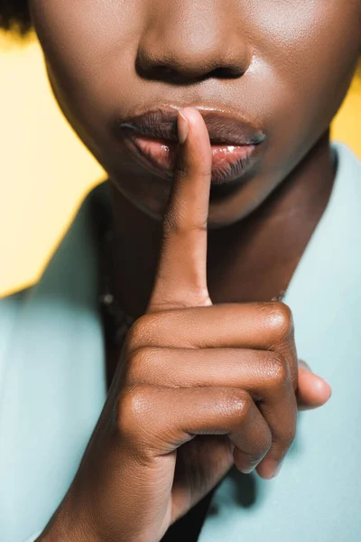 Cropped view of african american young woman in blue stylish outfit showing shh isolated on yellow — Stock Photo