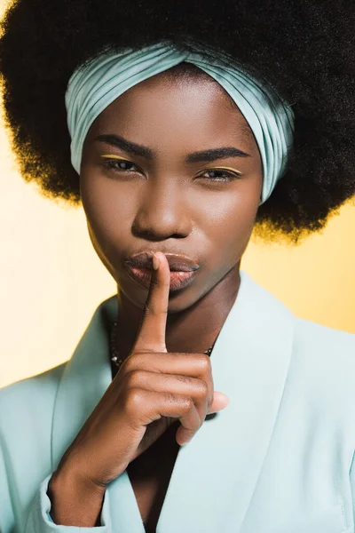 African american young woman in blue stylish outfit showing shh isolated on yellow — Stock Photo