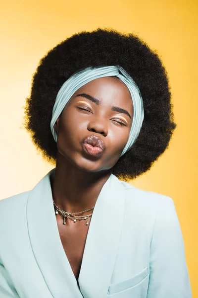 Afro americano jovem mulher no azul elegante roupa mostrando beijo isolado no amarelo — Fotografia de Stock