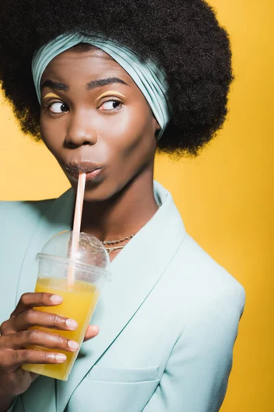 Mujer joven afroamericana en traje elegante azul con jugo de naranja aislado en amarillo - foto de stock