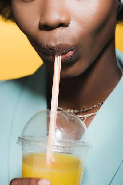 Ausgeschnittene Ansicht von afrikanisch-amerikanischen junge Frau in blau stilvolles Outfit mit Orangensaft isoliert auf gelb — Stockfoto