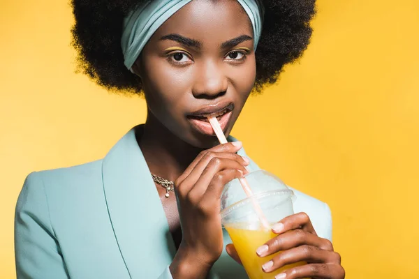 Mujer joven afroamericana en traje elegante azul con jugo de naranja aislado en amarillo - foto de stock