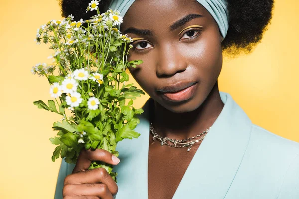 African american young woman in blue stylish outfit with chamomile bouquet isolated on yellow — Stock Photo