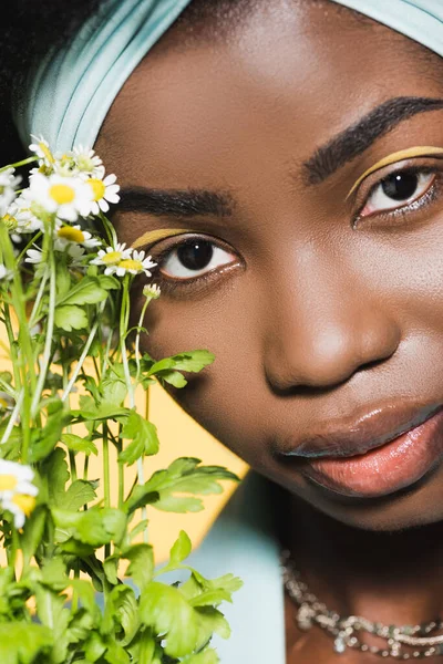 Primo piano della giovane donna afroamericana con bouquet di camomilla isolato su giallo — Foto stock