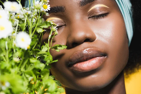 Gros plan de jeune femme afro-américaine avec bouquet de camomille isolé sur jaune — Photo de stock