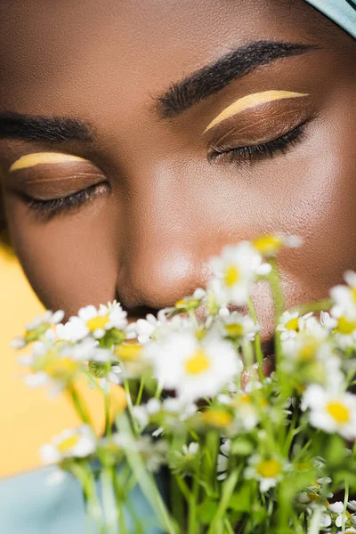 Nahaufnahme einer jungen afrikanisch-amerikanischen Frau mit Kamillenstrauß isoliert auf gelb — Stockfoto