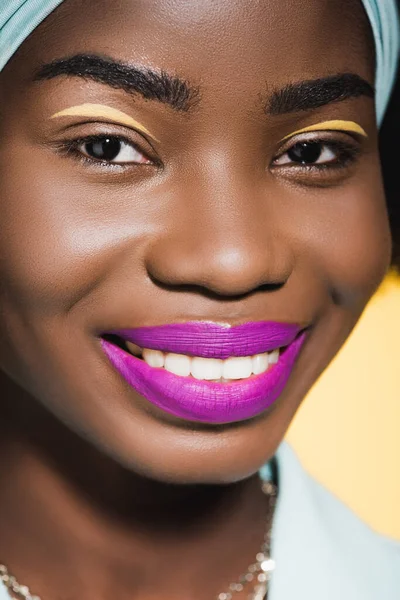 Усміхнена афроамериканська молода жінка з фіолетовими губами ізольована на жовтому — стокове фото