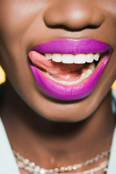 Vista ritagliata di afro-americana giovane donna con labbra viola mostrando lingua isolata sul giallo — Foto stock