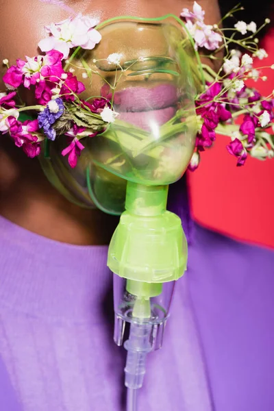 Cropped view of african american young woman in purple stylish outfit with flowers in inhaler isolated on red — Stock Photo
