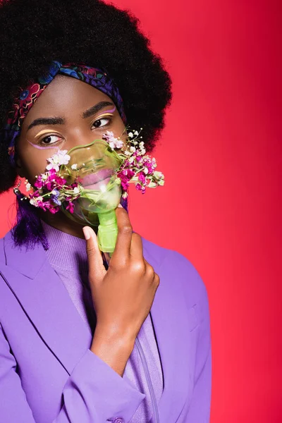 African american young woman in purple stylish outfit with flowers in inhaler isolated on red — Stock Photo