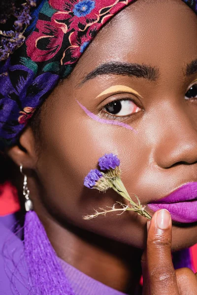 Closeup of african american young woman with purple flower isolated on red — Stock Photo