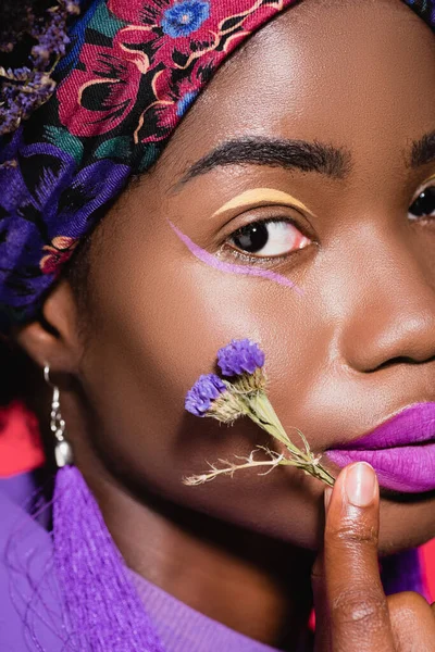 Primer plano de mujer joven afroamericana con flor púrpura aislada en rojo - foto de stock