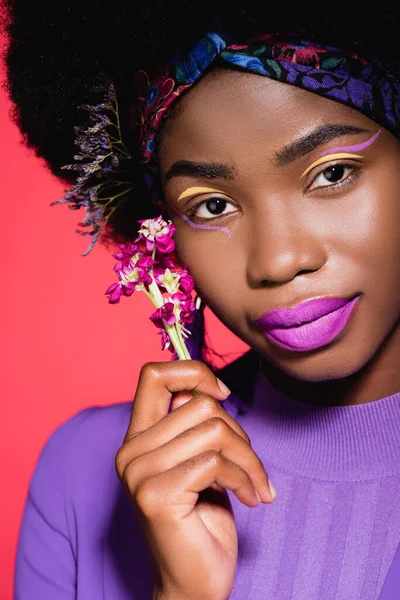 Mujer joven afroamericana en traje elegante púrpura con flor aislada en rojo - foto de stock