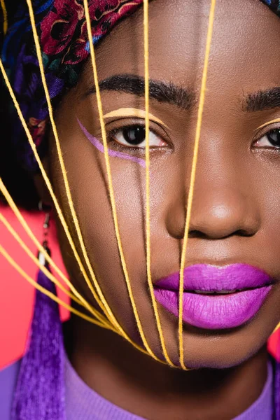 Afro-américaine jeune femme en costume violet élégant avec des cordes jaunes sur le visage isolé sur le rouge — Photo de stock