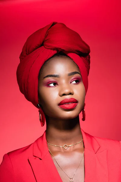 African american young woman in stylish outfit and turban isolated on red — Stock Photo