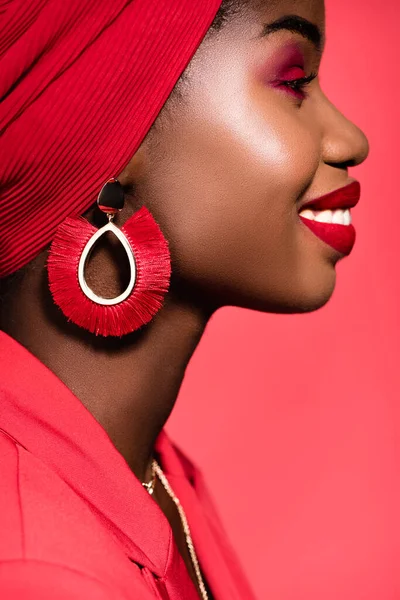 Perfil de la joven afroamericana sonriente en traje elegante y turbante aislado en rojo - foto de stock
