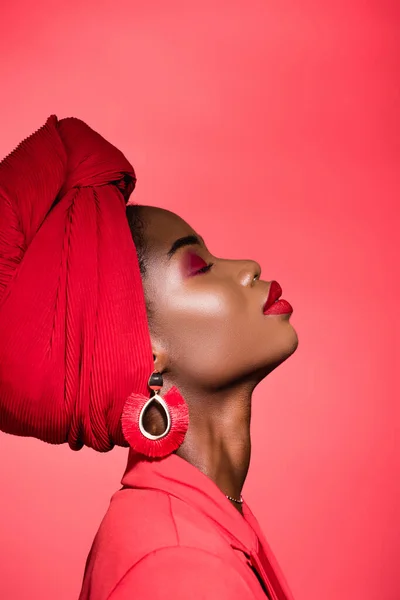 Profile of african american young woman in stylish outfit and turban with closed eyes isolated on red — Stock Photo