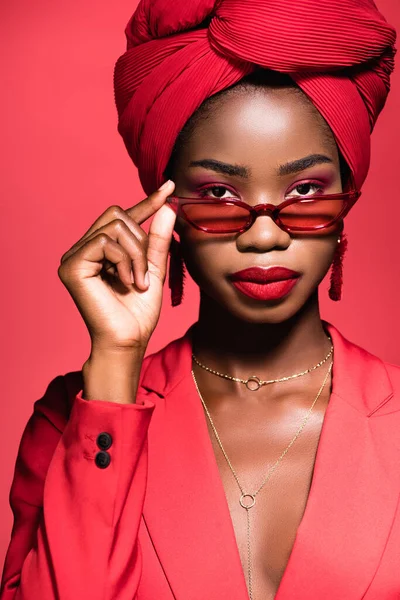 Africano americano giovane donna in abito elegante, occhiali da sole e turbante isolato su rosso — Foto stock