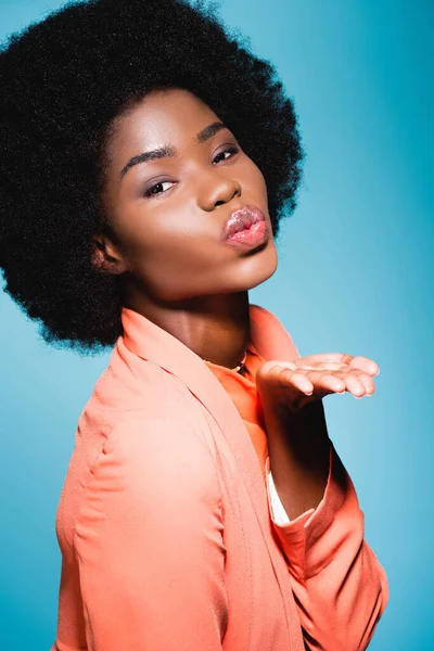 Africano americano joven mujer en naranja elegante traje soplado beso aislado en azul - foto de stock