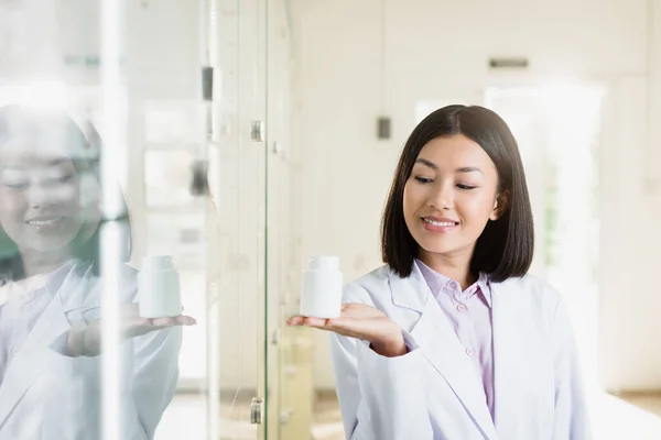 Heureux asiatique pharmacien dans blanc manteau pointant avec main dans drugstore — Photo de stock