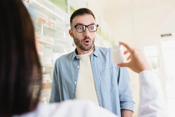 Cliente sorpreso guardando farmacista bottiglia con farmaco in primo piano offuscata — Foto stock