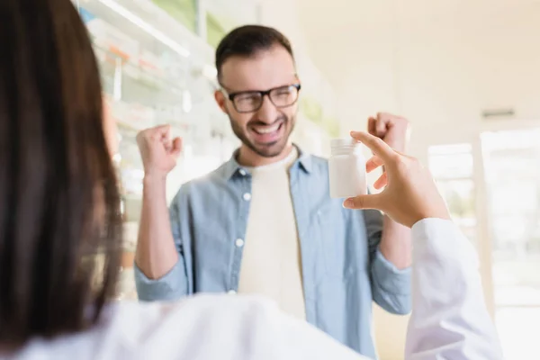 Excited customer looking at pharmacist holding bottle with medication on blurred foreground — Stock Photo