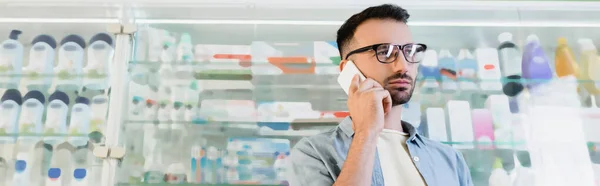 Man in eyeglasses talking on smartphone in drugstore, banner — Stock Photo
