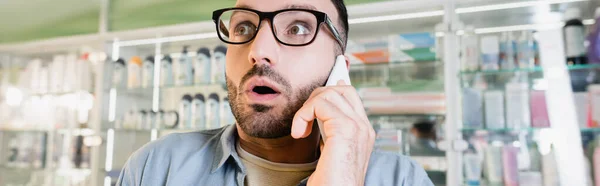 Sorprendido hombre en gafas hablando en el teléfono inteligente en la farmacia, pancarta - foto de stock