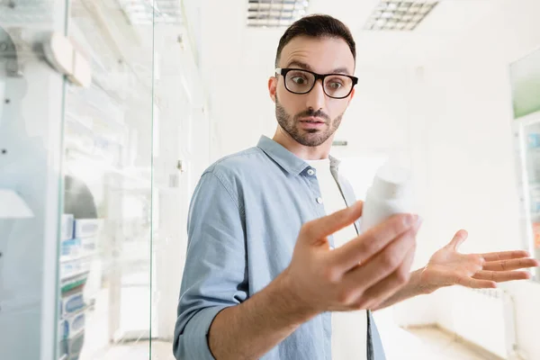 Homme surpris dans des lunettes tenant bouteille avec des pilules sur le premier plan flou — Photo de stock