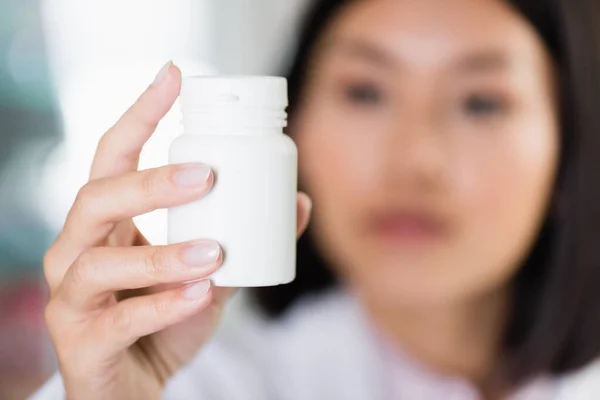 Bouteille avec des pilules en main du pharmacien asiatique sur fond flou — Photo de stock